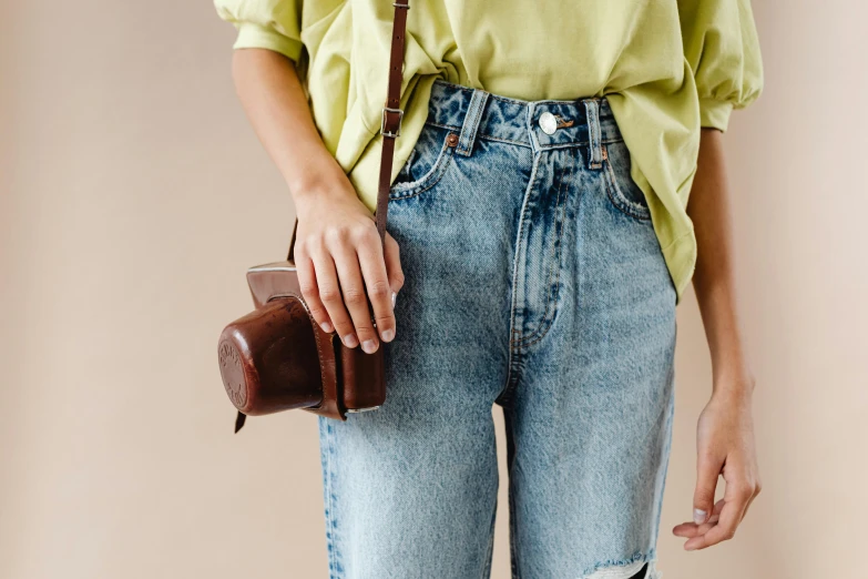 a woman in a green shirt is holding a brown purse, inspired by Jean Hey, trending on pexels, holding a tin can, denim jeans, 90s photo, chocolate