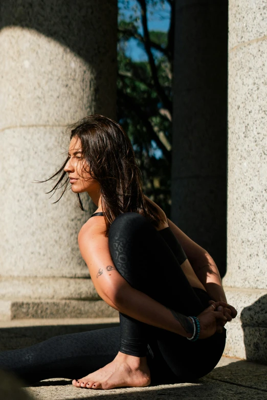 a woman sitting on the ground in front of a building, a statue, by Nina Hamnett, unsplash, arabesque, she is wearing a black tank top, standing athletic pose, afternoon light, black ponytail