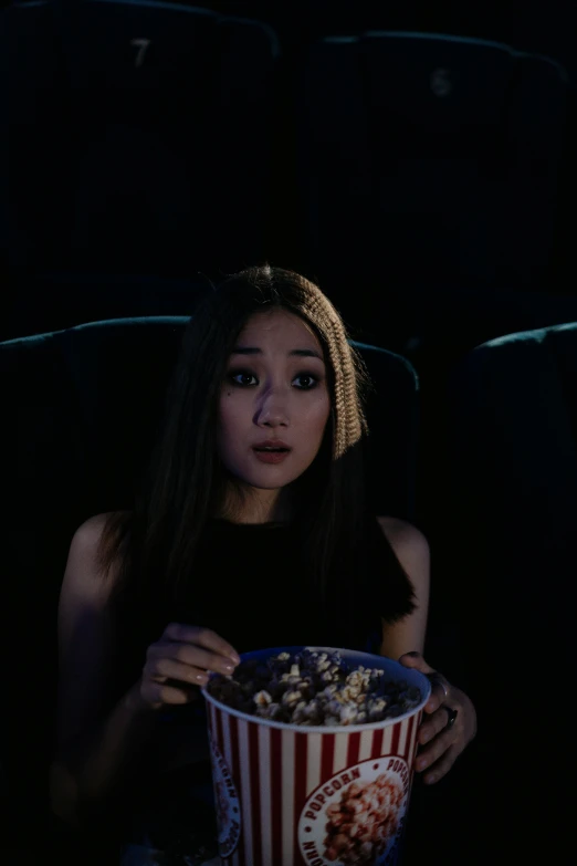 a woman sitting in a chair holding a bucket of popcorn, inspired by Gottfried Helnwein, tumblr, still from alita, half asian, having an awkward dinner date, sitting sad in spaceship