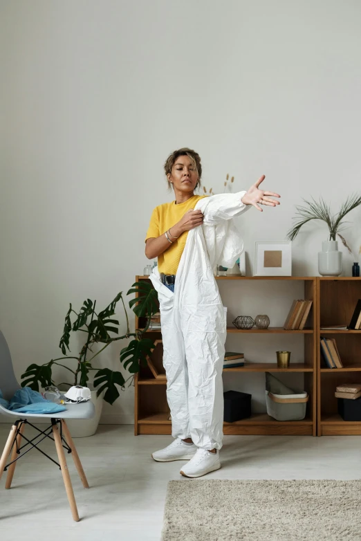 a woman standing in a living room holding a blanket, a statue, pexels contest winner, wearing human air force jumpsuit, stretching to walls, wearing lab coat, yellow overall