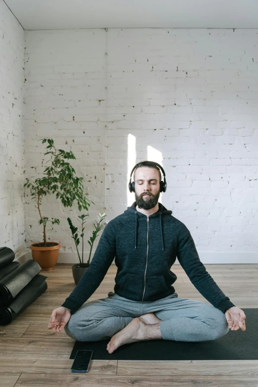 a man sitting on a yoga mat with headphones on, by Everett Warner, trending on pexels, light and space, low quality footage, album cover, wearing a headset, head is centered
