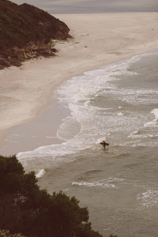 a man riding a surfboard on top of a sandy beach, down there, in the water, australian beach, grainy