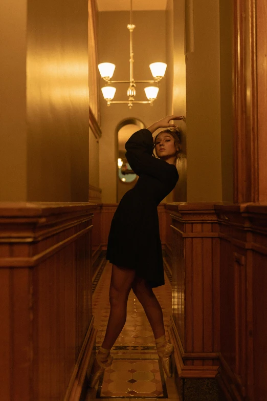 a woman in a black dress standing in a hallway, inspired by Nan Goldin, unsplash contest winner, renaissance, classic dancer striking a pose, lucy hale, ( ( theatrical ) ), sydney sweeney