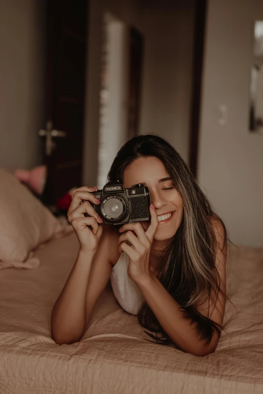 a woman laying on top of a bed holding a camera, beautiful and smiling, pixvy, trending on vsco, icon