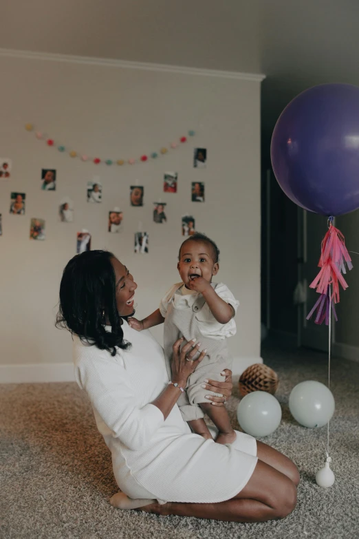 a woman sitting on the floor with a baby, a picture, by Dulah Marie Evans, pexels contest winner, party balloons, ( ( dark skin ) ), purple themed, a still of a happy