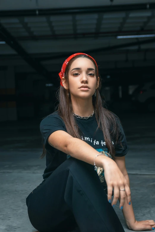 a woman sitting on the ground with a skateboard, by Robbie Trevino, red shirt, portrait of ariana grande, wearing black tshirt, bandana