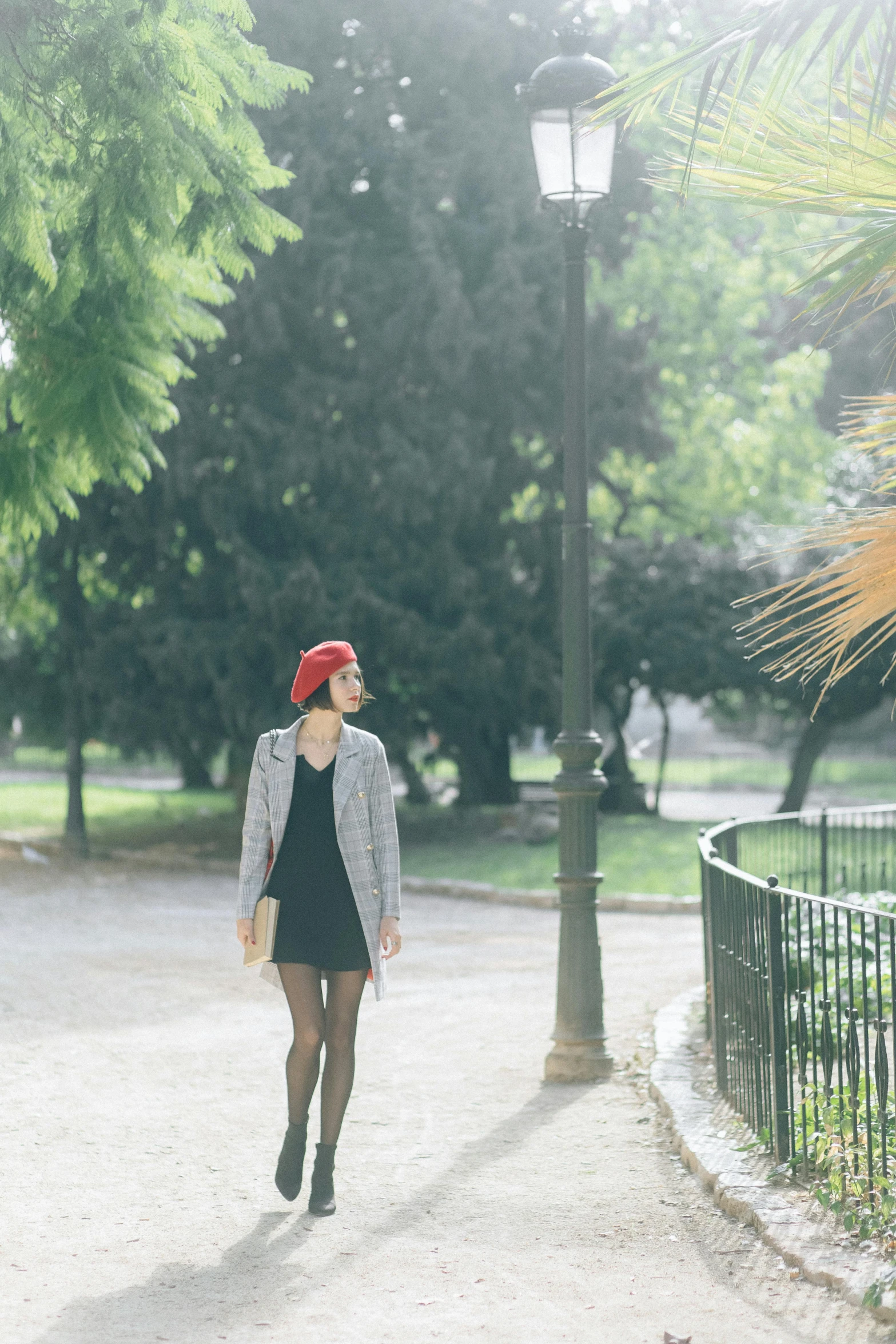 a woman walking down a path in a park, inspired by Oleg Oprisco, unsplash, wearing a french beret, black and red, in spain, street view