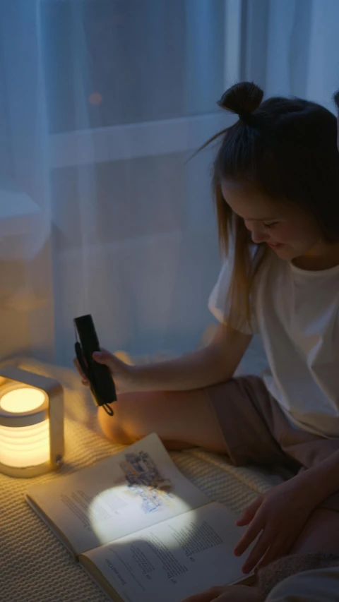 a little girl sitting on the floor reading a book, inspired by Isamu Noguchi, pexels contest winner, light and space, connected with glowing tubes 8 k, she is holding a smartphone, studyng in bedroom, table light