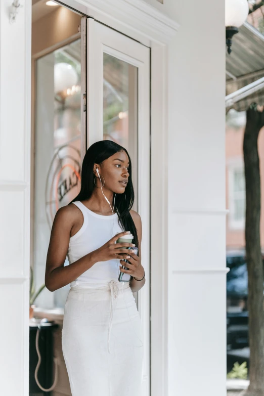 a woman standing outside of a building holding a cup of coffee, trending on pexels, earbuds jewelry, dark skin tone, transparent background, looking out window