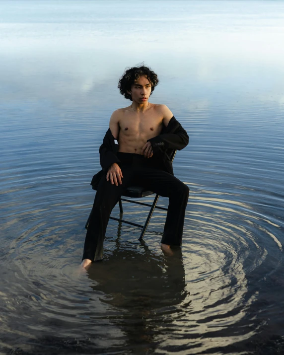 a man sitting in a chair in the water, an album cover, unsplash, renaissance, non binary model, an olive skinned, confident pose, robert sheehan