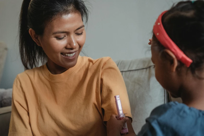 a woman sitting next to a little girl on a couch, pexels contest winner, hurufiyya, holding a syringe, profile image, smiling playfully, slightly tanned