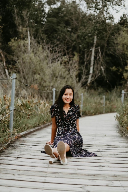 a woman sitting on top of a wooden walkway, a picture, inspired by helen huang, unsplash, happening, happily smiling at the camera, patterned, 1 6 years old, black