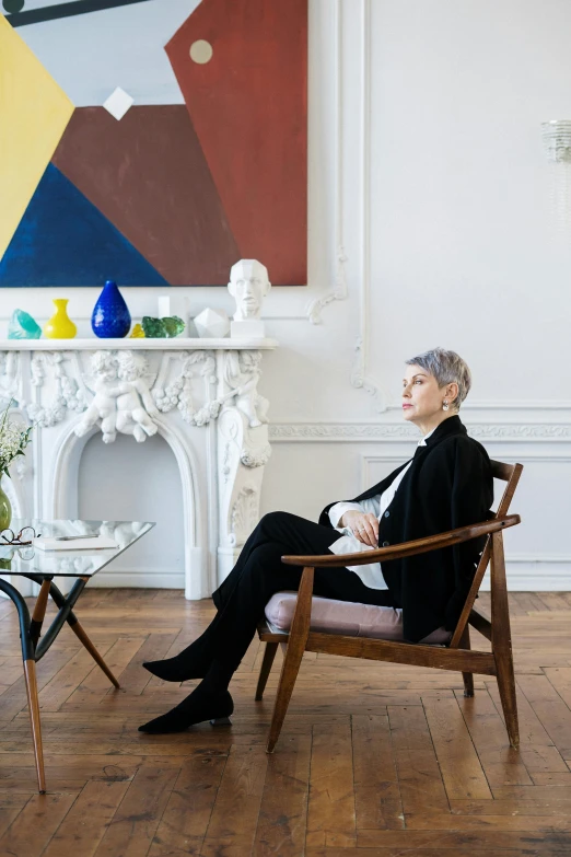 a woman sitting in a chair in front of a painting, inspired by Marie-Gabrielle Capet, visual art, short grey hair, architectural digest, lgbtq, ignant