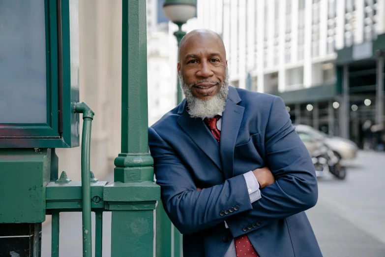 a man in a suit leaning against a green pole, an album cover, inspired by William H. Mosby, unsplash, renaissance, bald head and white beard, cityscape, looking straight to camera, he is about 50 years old