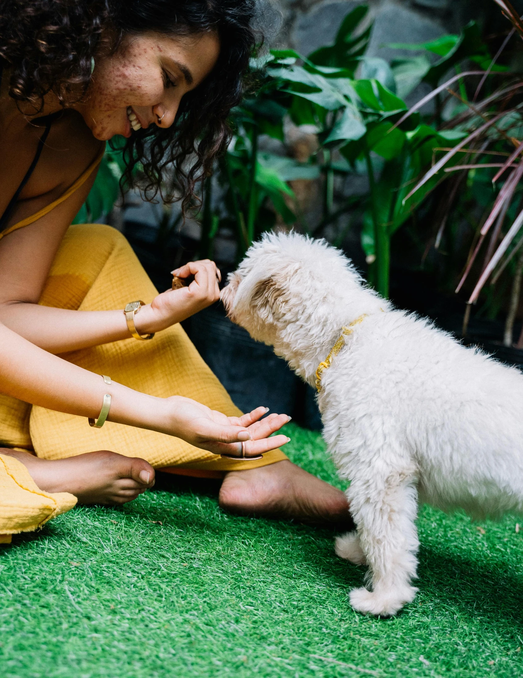 a woman petting a small white dog on the grass, by Julia Pishtar, trending on unsplash, bali, wearing yellow croptop, cafe for felted animals, thumbnail