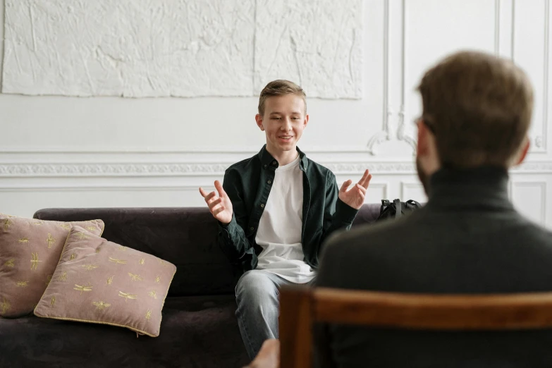 a man sitting on a couch talking to another man, pexels, young boy, inviting posture, promotional image, casey cooke