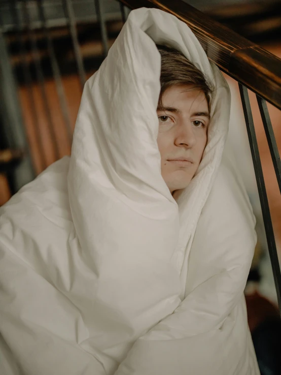 a close up of a person in a bed under a blanket, declan mckenna, profile image, wearing a white winter coat, haunted sad expression