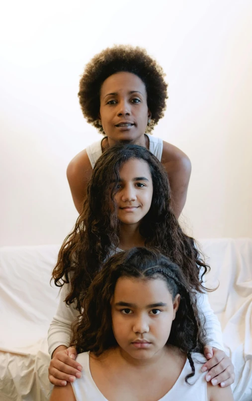 a group of young women sitting on top of a bed, by Nadir Afonso, antipodeans, close up portrait photo, portrait of family of three, mixed-race woman, head straight down