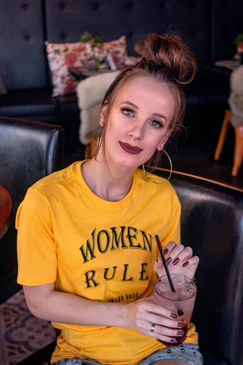 a woman in a yellow shirt sitting in a chair, trending on pexels, realism, golden rule, makeup, graphic tees, college girls