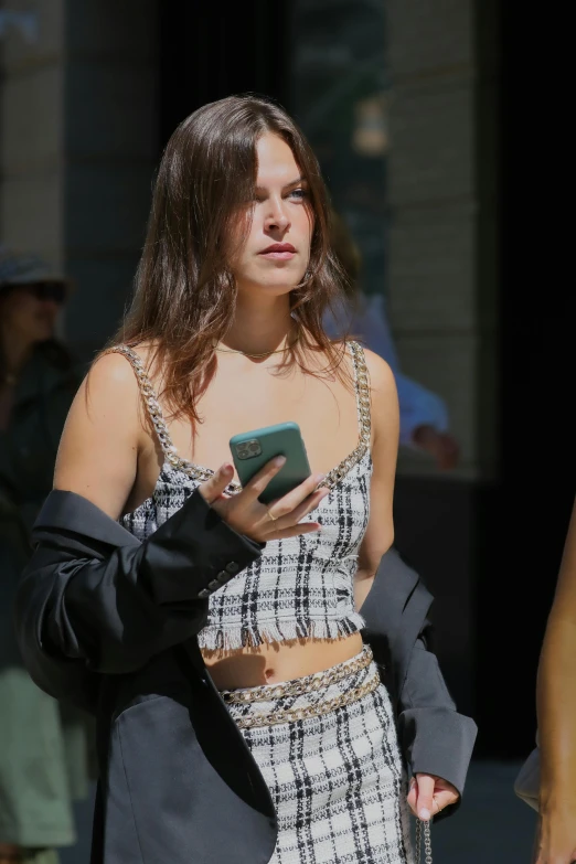 a woman walking down a street holding a cell phone, bella hadid, midriff, elisabeth moss, 2019 trending photo