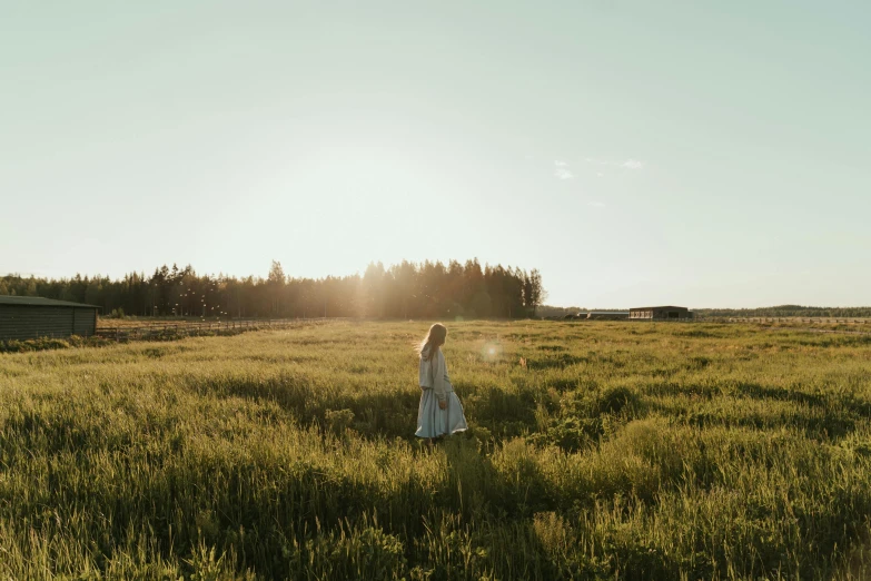 a woman standing in a field of tall grass, unsplash contest winner, land art, evening sun, forest setting in iceland, cottagecore hippie, sun puddle