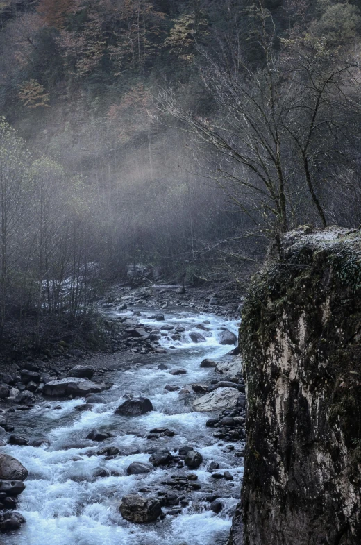 a man standing on top of a cliff next to a river, by Muggur, pexels contest winner, romanticism, winter mist around her, italy, small stream, panoramic