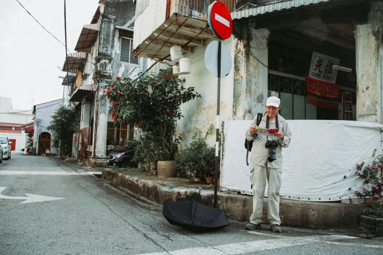 a man standing on the side of a street holding an umbrella, wearing a travel hat, film shooting, bao pnan, exploration