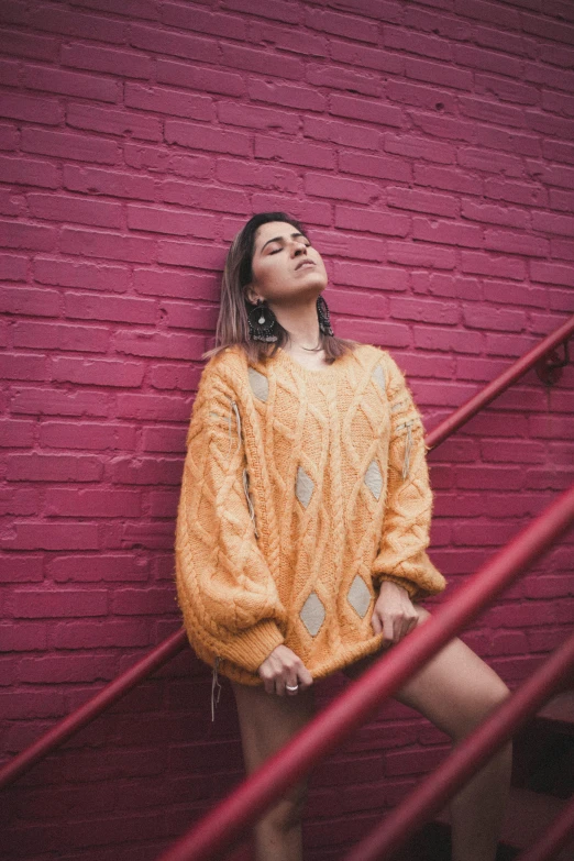 a woman standing in front of a brick wall, an album cover, inspired by Elsa Bleda, trending on pexels, wearing an oversized sweater, beautiful yellow woman, 5 0 0 px models, orange