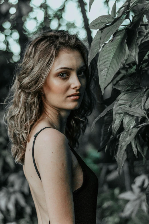 a beautiful young woman standing in front of a tree, inspired by Elsa Bleda, pexels contest winner, renaissance, lush jungle, wavy hairstyle, she is wearing a black tank top, desaturated color