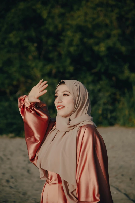 a woman standing on top of a sandy beach, an album cover, inspired by Maryam Hashemi, pexels contest winner, hurufiyya, greeting hand on head, in a park, hijab, high quality screenshot