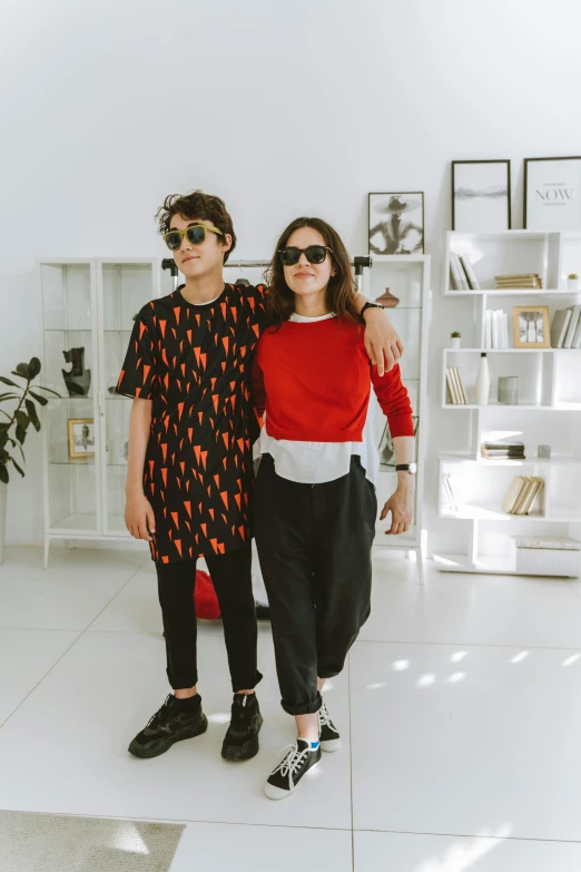 two people standing next to each other in a room, by Julia Pishtar, wearing cool sunglasses, red and black colors, teen boy, at home