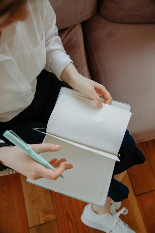 a woman sitting on a couch reading a book, trending on unsplash, blue ballpoint pen, wearing a white shirt, luxury journal cover, pastel colored