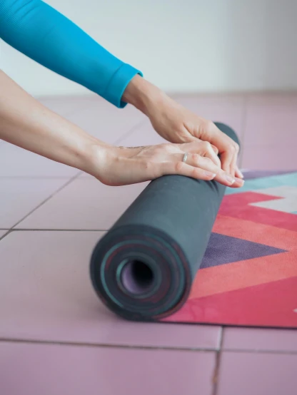 a woman rolling up a yoga mat on the floor, by Rachel Reckitt, close - up photograph, multicoloured, matte fresco, large format