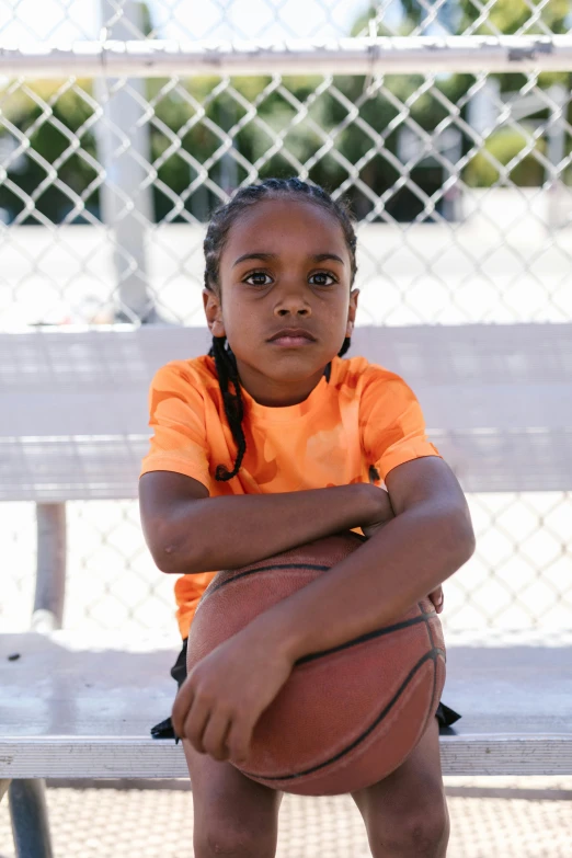 a young girl sitting on a bench holding a basketball, by Gavin Hamilton, dribble contest winner, : kendrick lamar, looking to camera, orange, serious expression