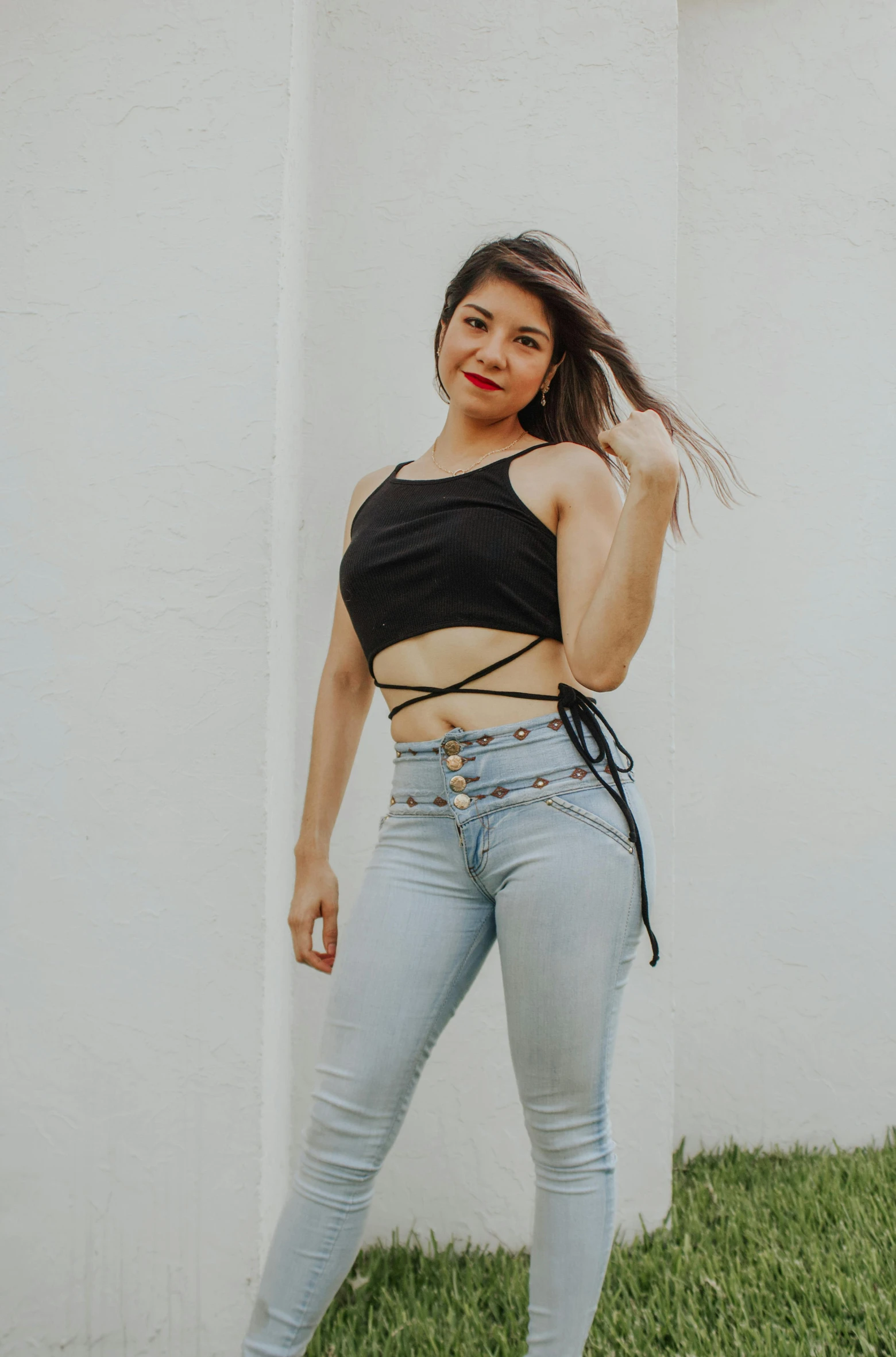 a woman standing in front of a white wall, by Robbie Trevino, trending on pexels, renaissance, wearing a cropped black tank top, ( ( ( wearing jeans ) ) ), cables, colombian