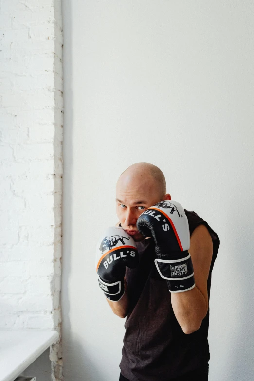 a man standing in front of a window wearing boxing gloves, inspired by Daryush Shokof, bald head, mma southpaw stance, profile image, jovana rikalo