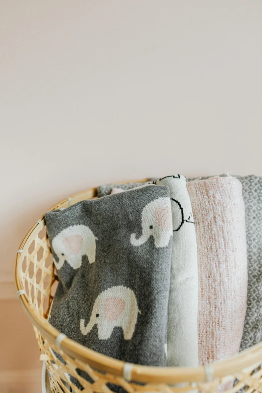 a basket that has some blankets in it, a picture, by Will Ellis, trending on unsplash, mingei, cute elephant, pink and grey muted colors, panel, delicate patterned