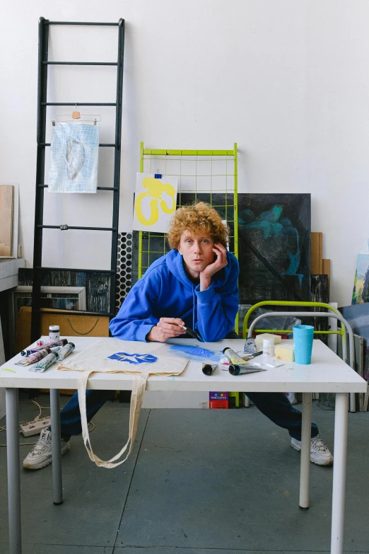 a man sitting at a table talking on a cell phone, a portrait, by Penelope Beaton, sophia lillis, in a studio, artist wearing overalls, adafruit