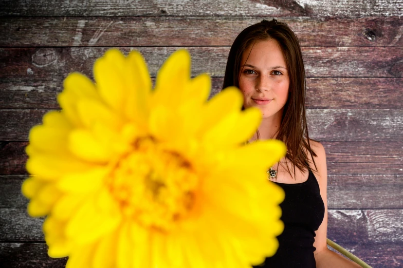 a woman holding a yellow flower in front of a wooden wall, a portrait, by Matthias Stom, pixabay contest winner, avatar image, no cropping, dafne keen, indoor picture