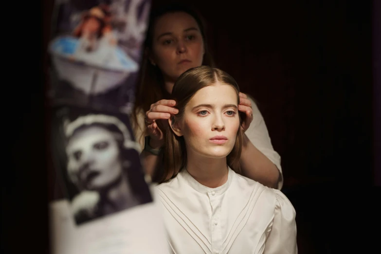 a woman getting her hair done in front of a mirror, by Emma Andijewska, film promotional still, her face is coated in a white, hammershoi, fashion week backstage