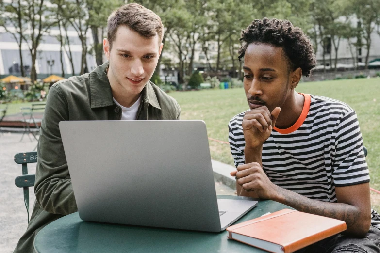 two men sitting at a table looking at a laptop, trending on pexels, in a park, college students, teaching, multicoloured