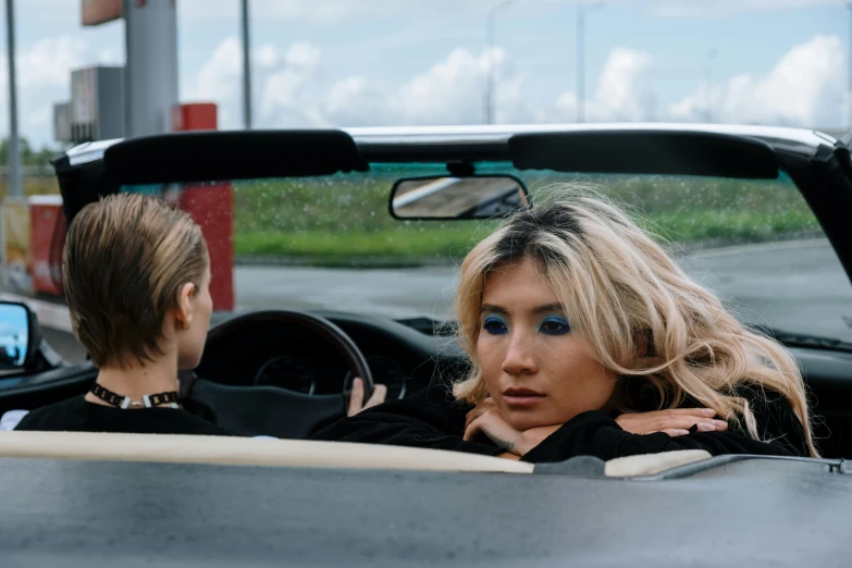 a woman sitting in the driver's seat of a convertible car, inspired by Elsa Bleda, trending on pexels, visual art, two models in the frame, messy blond hair, oil slick, julia sarda
