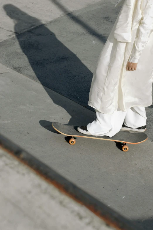 a person in a white robe riding a skateboard, large pants, zoomed out to show entire image, white shoes, religious