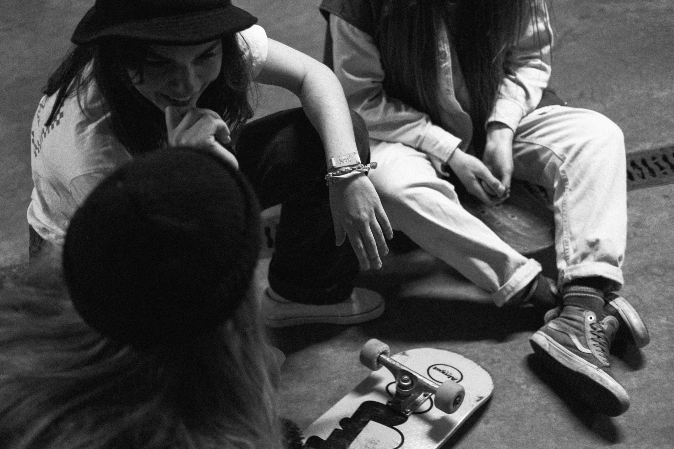 a group of people sitting on the ground with skateboards, a black and white photo, by Emma Andijewska, unsplash, process art, young girls, indoor shot, holding court, mechanics