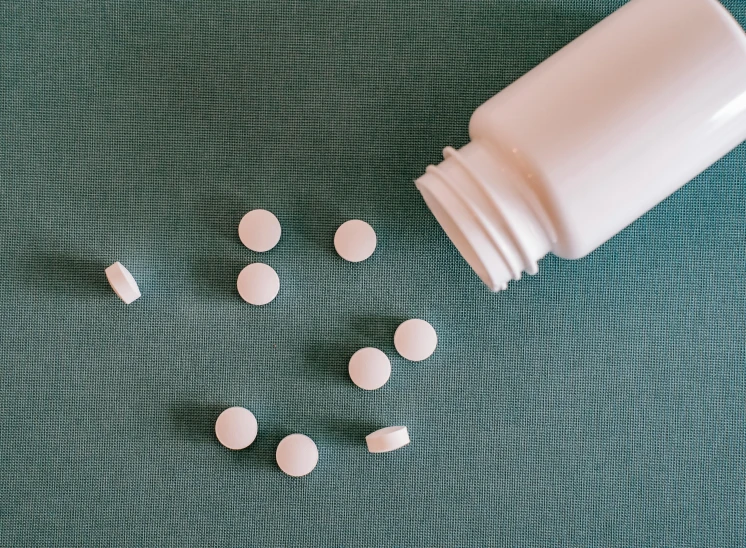 a close up of a bottle of pills on a table, by Amelia Peláez, pexels contest winner, white and teal garment, hdpe, minimalist photorealist, white pearlescent