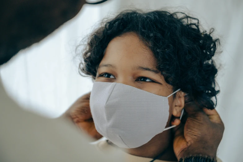 a man putting a mask on a woman's face, by Emma Andijewska, pexels contest winner, hurufiyya, kids, closeup of an adorable, avatar image, grey