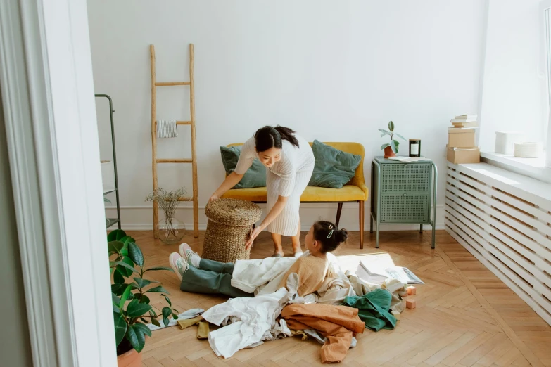 a woman sitting on the floor next to a little girl, by Emma Andijewska, pexels contest winner, furniture overturned, working clothes, filled with plants, gif