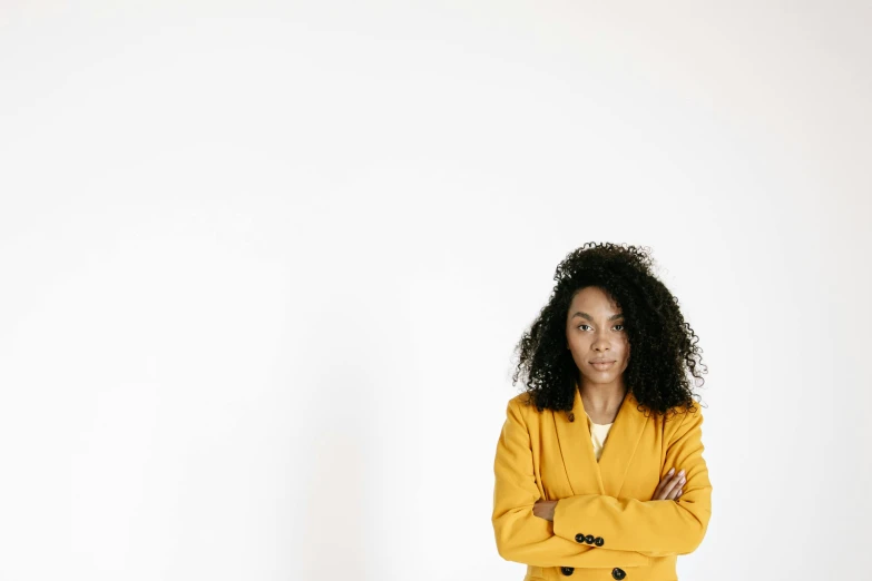 a woman standing with her arms crossed in front of a white wall, pexels, yellow carpeted, wearing jacket, mixed-race woman, complaints