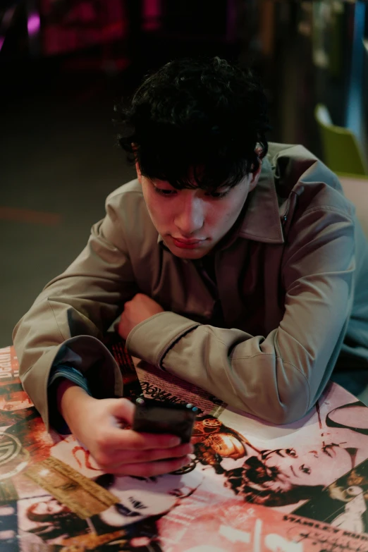 a man sitting at a table with a cell phone, an album cover, inspired by Nan Goldin, trending on pexels, hyperrealism, finn wolfhard, concentrated, high quality photo, concert