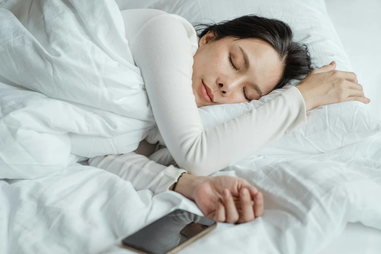 a woman laying in bed next to a cell phone, trending on pexels, wearing a white sweater, sleeping beauty, an asian woman, walking down